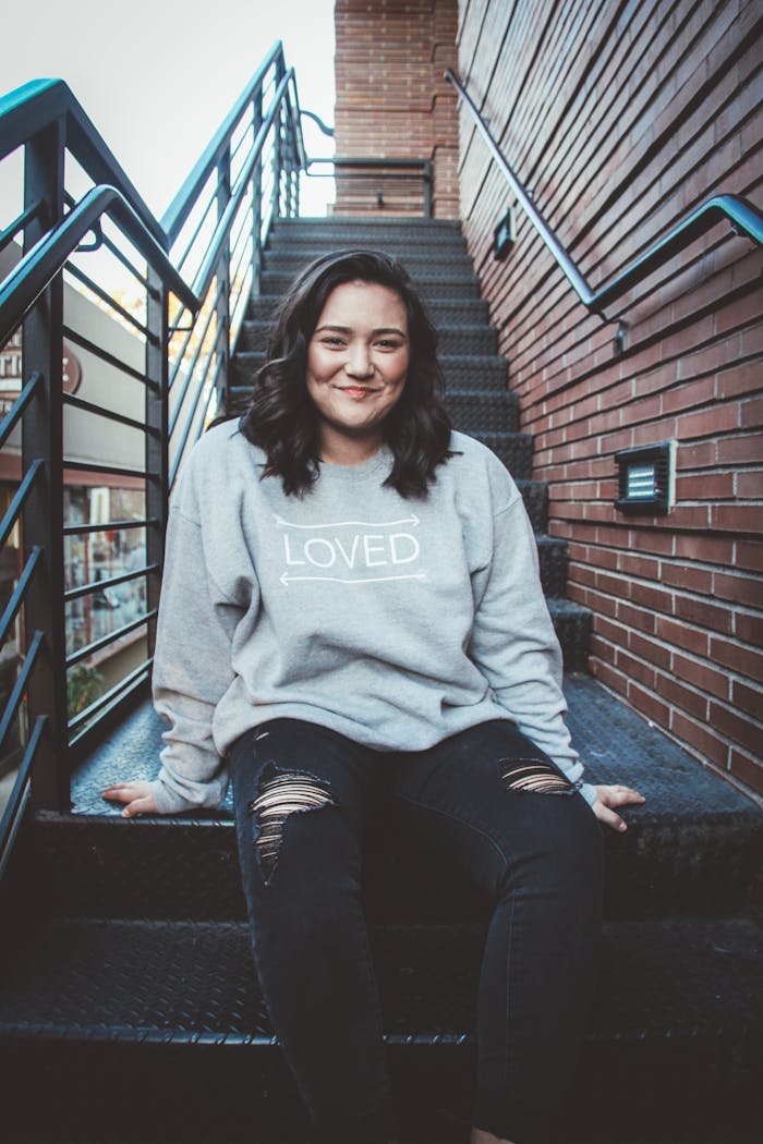 Portrait of a smiling woman sitting on outdoor stairs in casual attire.