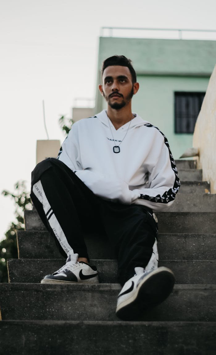 journey A stylish young man wearing streetwear sits on steps outdoors, embodying modern urban fashion.